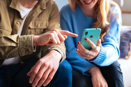 A surprised woman and a smiling man looking at a smartphone, sharing an exciting moment together. Both holding phones, seated indoors, with cheerful expressions of joy and amazemen