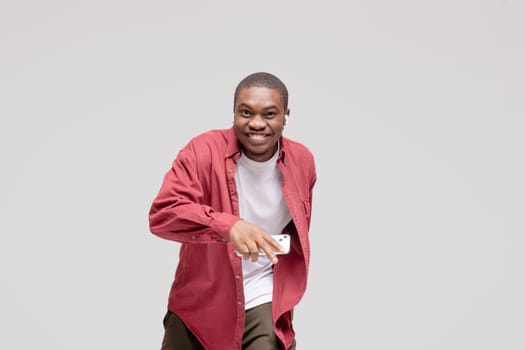 young African American man pictured isolated on gray background wearing casual clothes and hat dancing to music he is listening through wireless earphones, feeling relaxed and happy