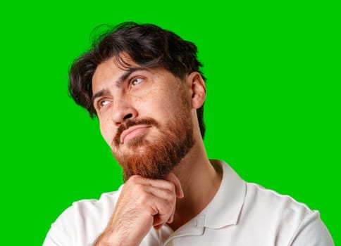 A man contemplates thoughtfully against a bright green background in studio
