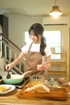 Cropped shot of young woman cooking, stirring ingredients in frying pan with spatula.