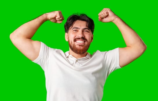 Happy man celebrating success with raised fists, wearing a white shirt against a bright green background close up