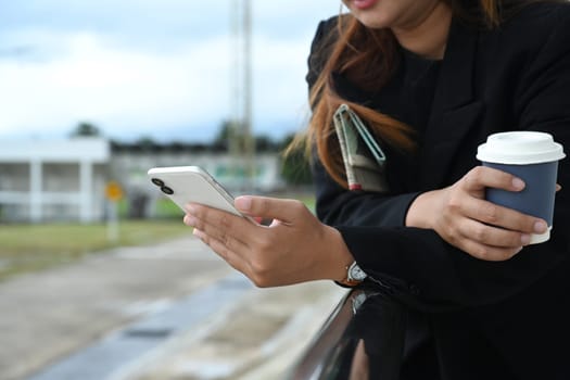 Young businesswoman with a cup of coffee leaning on the railing and using mobile phone.