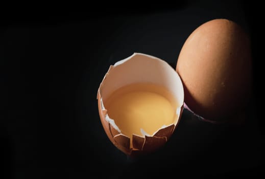View of Egg yolk in Broken raw chicken eggshell and Fresh chicken egg (Hen egg) on Black background. Fresh eggs from the farmer, Natural organic healthy food concept, Space for text, Selective focus.