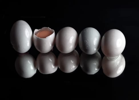 Five raw duck eggs are sitting in a row with an egg broken in half showing the yolk and white egg with reflection on dark background. use it as your Wallpaper, Poster and Space for text, Selective focus.