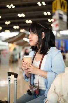 Young woman with a coffee cup waiting for her flight at the airport.