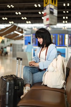 Smiling young woman working on laptop while waiting for flight in airport.