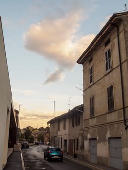 Cremona, Italy September 26th 2024 A blue car is driving down a narrow street in an italian village at sunset, with old buildings and a cloudy sky