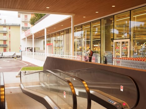 Cremona, Italy September 26th 2024 Modern supermarket with glass walls and escalators leading to the entrance with a customer entering