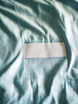 A plain white rectangular label on a wrinkled light blue fabric surface, creating a soft and serene aesthetic.