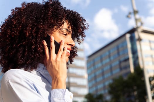 close up portrait of a female entrepreneur with curly hair talking on smart phone at city