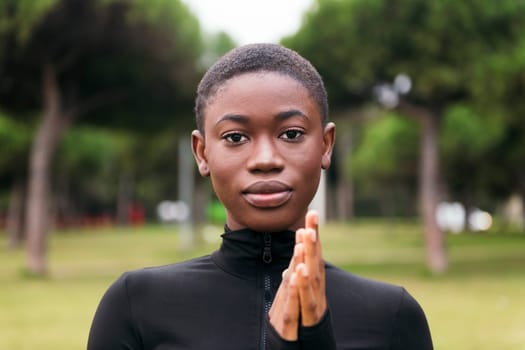 young tender ethnic female in black apparel with short hair looking at camera on urban lawn in summer