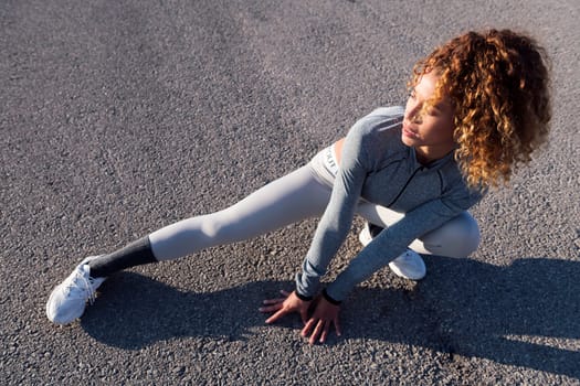 adult female athlete in sportswear performing side squat during training on asphalt roadway, concept of urban sport and healthy lifestyle