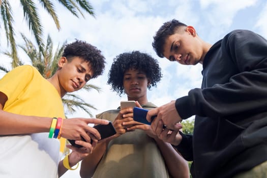 low angle of teen diverse friends having fun surfing Internet on cellphones at park, concept of youth lifestyle and technology of communication