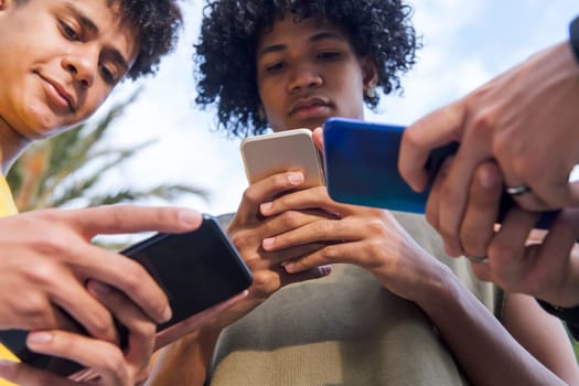 close up of teen diverse friends having fun surfing Internet on cellphones at park, concept of youth lifestyle and technology of communication