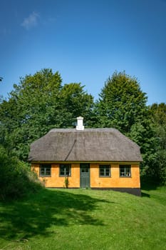 A picturesque orange cottage with a traditional thatched roof surrounded by lush greenery under a clear blue sky. Perfect depiction of rural tranquility and rustic charm.