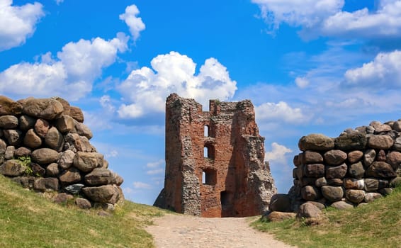A weathered stone tower stands amid rolling hills, framed by ancient rock walls under a bright blue sky with fluffy clouds, inviting exploration and reflection on history.