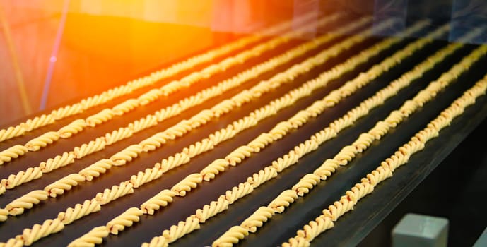 Long rows of pasta shapes are being created on a production line in a factory setting. The process highlights the precision and efficiency of modern pasta manufacturing.