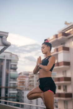 An individual who is highly focused is practicing yoga amidst a vibrant urban landscape as the sun sets