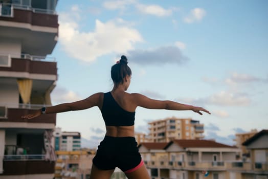 A woman is skillfully practicing yoga on a rooftop, fully enjoying the beautiful, serene city skyline and fresh air