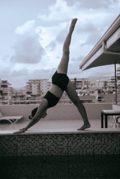A woman elegantly performs a yoga pose on a rooftop, with a vast cityscape behind her, embodying strength
