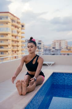 A woman skillfully practicing yoga poses by a serene pool on a scenic rooftop, embodying both tranquility and fitness