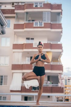 A woman gracefully performs yoga alongside a pool, beautifully emphasizing urban living alongside fitness mindfulness
