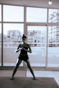 A focused young woman confidently strikes a challenging yoga pose in a bright, modern studio with stunning urban views