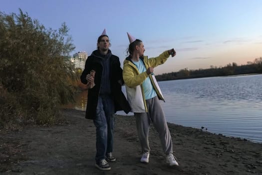 Celebrating friendship by the riverside at dusk with laughter, hats, and snacks during a joyful holiday gathering