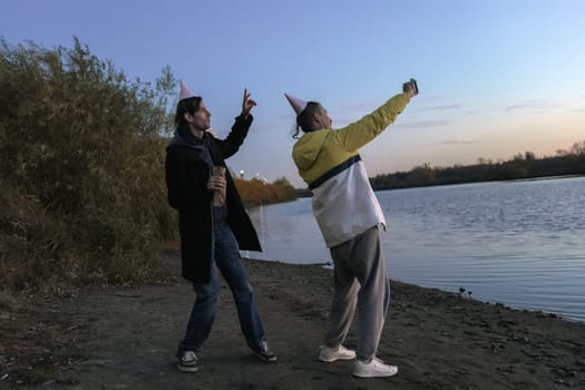 Two friends celebrating a holiday by the water at sunset, capturing joyful moments with festive hats and laughter in the air