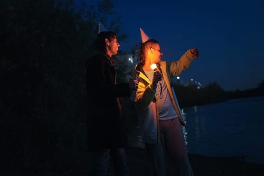 Two friends enjoy a memorable holiday evening by the water, laughing and sharing stories as they light the night with candles