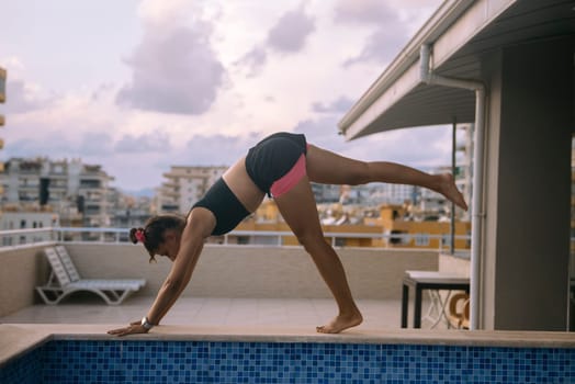 A young woman showcases her impressive yoga pose at a stunning rooftop pool featuring a breathtaking city view