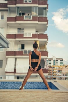 A confident woman poses by the poolside in an urban setting, beautifully showcasing her strength and elegance
