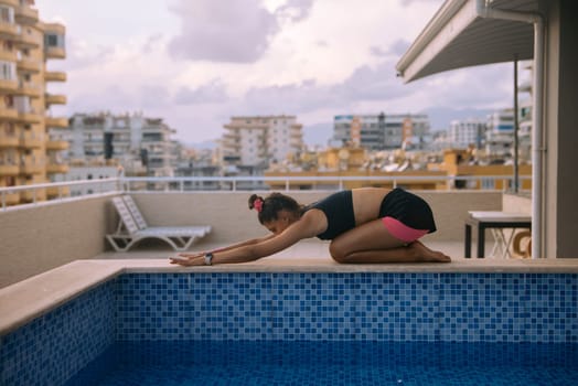 A woman performs a tranquil yoga pose by a serene pool in a busy urban area, showcasing her fitness and peace