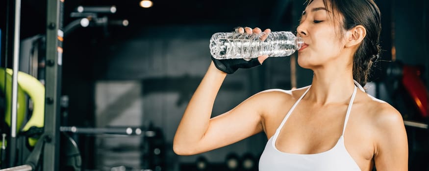 Asian woman guy hydrated by drinking water sports from a bottle in gym after cardio work out, female tired with liquid bottle drink after training at fitness gym, workout healthy lifestyle concept