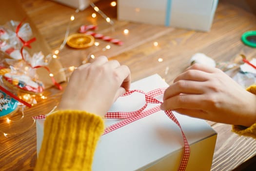 Christmas composition with present box. The girl ties a red ribbon on the gift box.