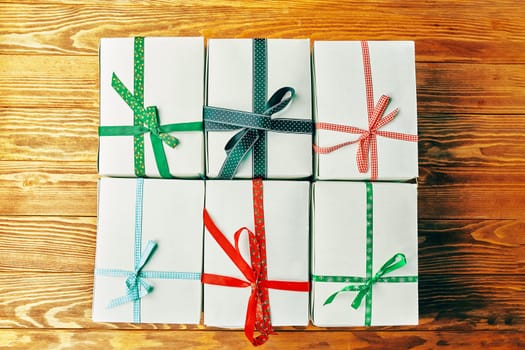 Stack of gift wrapped Christmas presents. A stack of gifts of white colors tied with different ribbons on a wooden background.
