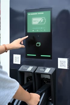 Young woman interacting with touchscreen interface of the charging station.