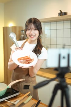 Cheerful young woman recording a cooking tutorial in a modern kitchen.