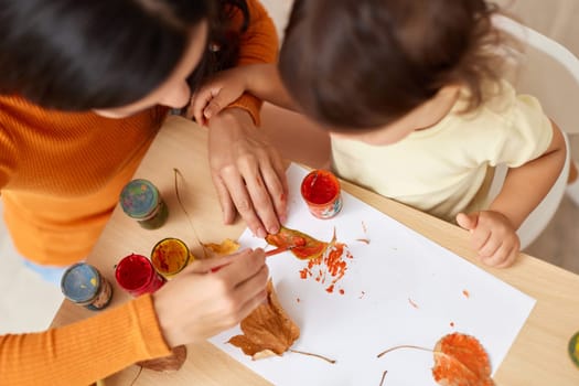 happy little child girl and her mother drawing for the autumn holiday. Autumn craft