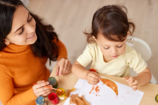 happy little child girl and her mother drawing for the autumn holiday. Happy family making autumn decorations together