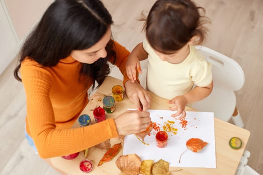 Cute little girl and mom spending good time painting autumn yellow leaves together