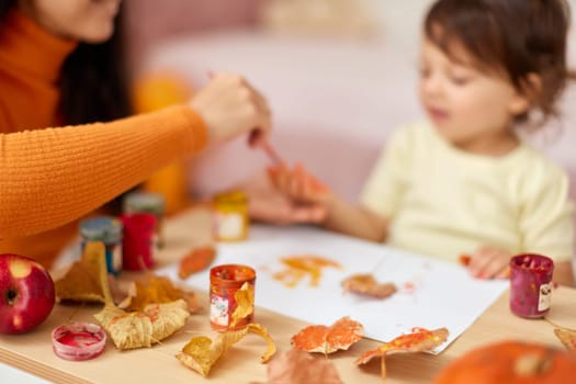 close-up, child and mom hands painting autumn yellow leaves together. happy time together at home