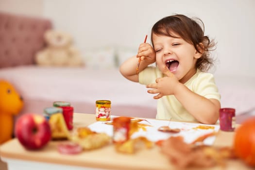 happy little child girl painting autumn leaves. smiling baby girl drawing leaves in yellow paint