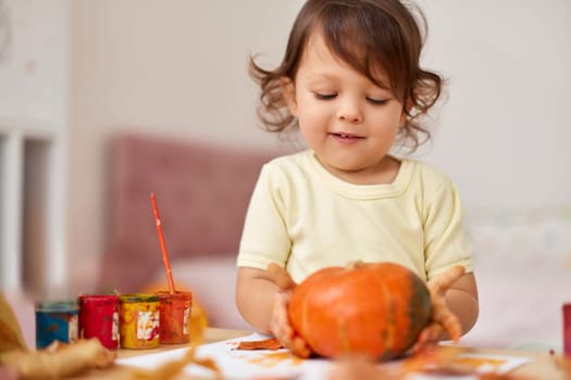 happy little child girl painting Halloween pumpkin. smiling baby girl drawing autumn pumpkin in yellow paint