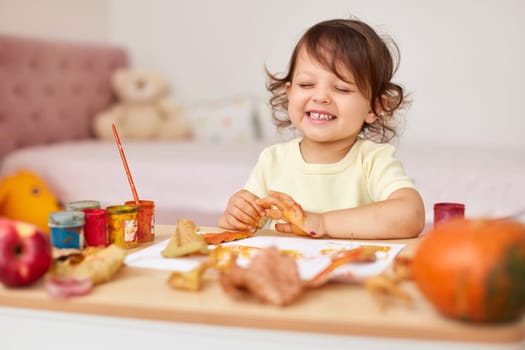happy little baby girl painting autumn leaves. baby girl drawing leaves in yellow and orange paint