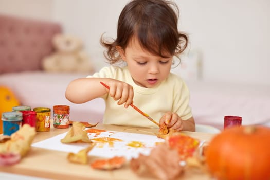 cute little child girl painting autumn leaves. baby girl drawing leaves in yellow and orange paint