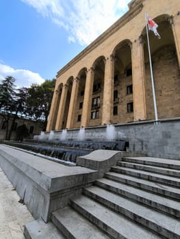 18 August 2024 Tbilisi Georgia modern building in the city center, gray stone stre fontaine, flag. High quality photo