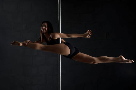 Sexy brunette in top and shorts exercising on pylon view in dark room
