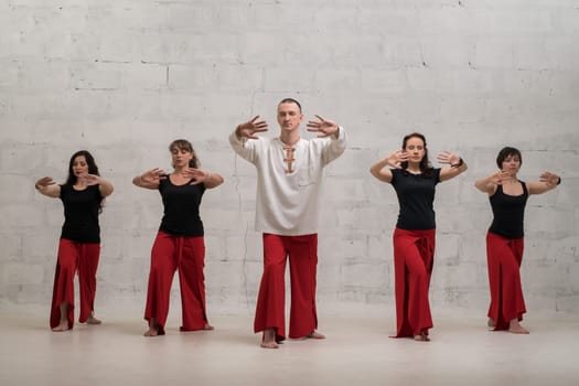 Group of women and their male trainer doing yoga exercises view against brick wall