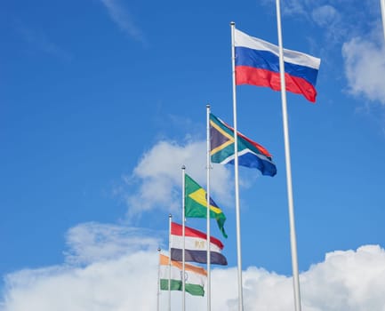 The flag of Russia and other countries is fluttering in the wind as a symbol of friendship and cooperation against the blue sky. Various national flags are flying on the flagpoles